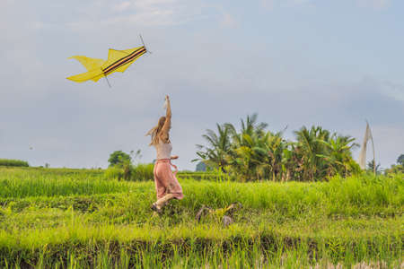 Young woman launches a kite in a rice field in Ubud, Bali Island, Indonesiaの写真素材