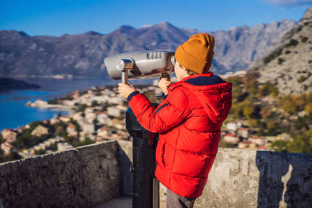 Young tourist boy boy looking through binoculars enjoying a view of Kotor Bay, Montenegro. Kotor Old...