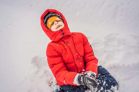 Funny little boy in blue winter clothes walks during a snowfall. Outdoors winter activities for kids. Cute child wearing a warm hat low over his eyes catching snowflakes with his tongueの写真素材