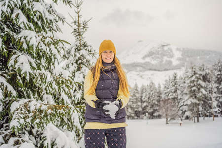 Happy pretty caucasian young woman in warm clothes and hat standing in blue snowy forest and looking...