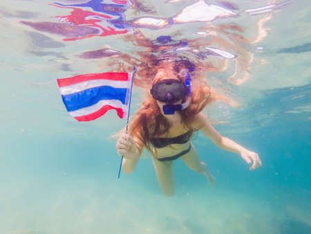 Happy woman in snorkeling mask dive underwater with tropical fishes with thailand flag in coral reef...