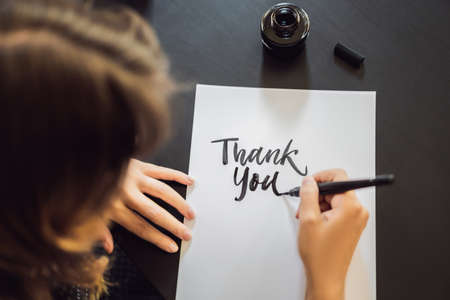 Thank you. Calligrapher Young Woman writes phrase on white paper. Inscribing ornamental decorated letters. Calligraphy, graphic design, lettering, handwriting, creation conceptの写真素材