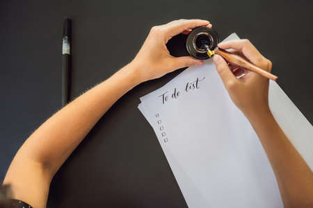 To do list. Calligrapher Young Woman writes phrase on white paper. Inscribing ornamental decorated letters. Calligraphy, graphic design, lettering, handwriting, creation conceptの写真素材
