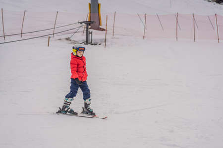 Child skiing in mountains. Active toddler kid with safety helmet, goggles and poles. Ski race for young children. Winter sport for family. Kids ski lesson in alpine school. Little skier racing in snowの写真素材