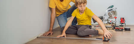 BANNER, LONG FORMAT Father and son installing new wooden laminate flooring on a warm film floor. Infrared floor heating system under laminate floorの写真素材