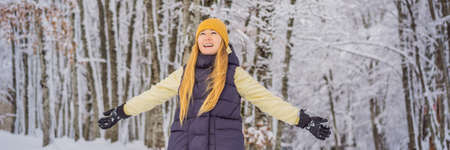 BANNER, LONG FORMAT Happy pretty caucasian young woman in warm clothes and hat standing in blue snowy forest and looking away. Smiling cute girl enjoying sunny day in winter, outdoorsの写真素材