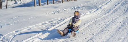 BANNER, LONG FORMAT Happy woman having fun during rolling down the mountain slope on sled. Winter...