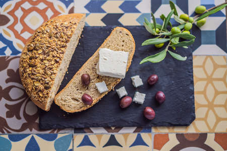 Green and black olives with loaf of fresh bread, feta cheese and young olives branch on olive wood...