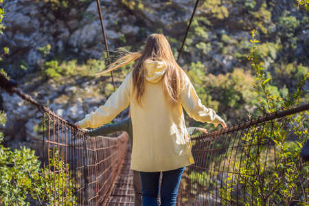 Woman tourist on Old rusty bridge. Attraction Long extreme suspension iron bridge across the river Moraca. Sights of Montenegro. Landmark Montenegroの写真素材