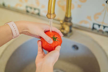 Close-up Of A Woman Washing Tomato In Running Water Under Tapの写真素材