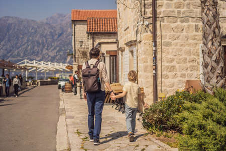 Dad and son tourists enjoying Colorful street in Old town of Perast on a sunny day, Montenegro. Travel to Montenegro concept. Scenic panorama view of the historic town of Perast at famous Bay of Kotor on a beautiful sunny day with blue sky and clouds in summer, Montenegro, southern Europe.の写真素材