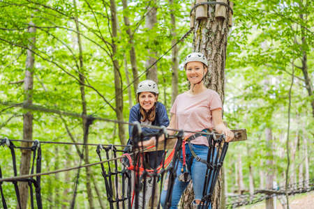 Two women girls female gliding climbing in extreme road trolley zipline in forest on carabiner safety link on tree to tree top rope adventure park. Family weekend children kids activities conceptの写真素材