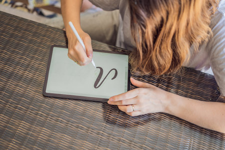 Calligrapher Young Woman writes phrase on digital tablet. Inscribing ornamental decorated letters. Calligraphy, graphic design, lettering, handwriting, creationの写真素材