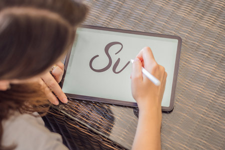 Calligrapher Young Woman writes phrase on digital tablet. Inscribing ornamental decorated letters. Calligraphy, graphic design, lettering, handwriting, creationの写真素材