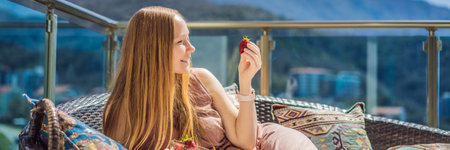 Portrait of gorgeous woman wearing beautiful dress sitting in a patio and eating strawberry BANNER, LONG FORMATの写真素材