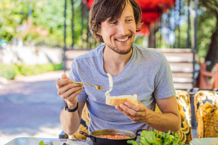 man tourist eat Turkish breakfast. Turkish breakfast table. Pastries, vegetables, greens, olives, cheeses, fried eggs, spices, jams, honey, tea in copper pot and tulip glasses, wide compositionの写真素材