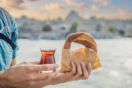 Man in Istanbul having breakfast with Simit and a glass of Turkish tea. Glass of Turkish tea and bagel Simit against golden horn bay in Istanbul, Turkey. Turkiyeの写真素材