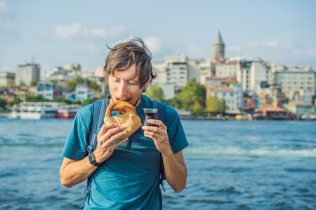 Man in Istanbul having breakfast with Simit and a glass of Turkish tea. Glass of Turkish tea and bagel Simit against golden horn bay and the Galata Tower in Istanbul, Turkey. Turkiyeの写真素材