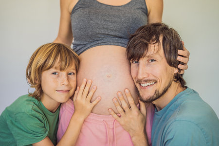 Father and elder son listen to moms pregnant bellyの写真素材