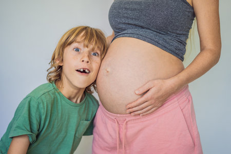 Young beautiful pregnant woman and eldest son. The cute boy leaned his ear against his mothers...