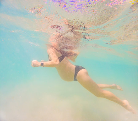 Pregnant woman underwater swimming in tropical sea. Healthy and active pregnancy. Young expecting mom on summer beach vacation before baby birth. Swim holiday and water fun. Travel during pregnancy. Underwater photographyの写真素材