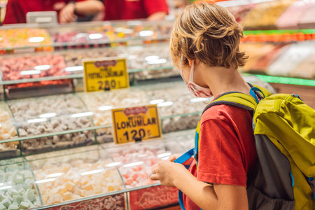 The boy looks at the counter with Turkish sweets. Traditional oriental sweet pastry cookies, nuts, dried fruits, pastilles, marmalade, Turkish desert with sugar, honey and pistachio, in display at a street food marketの写真素材