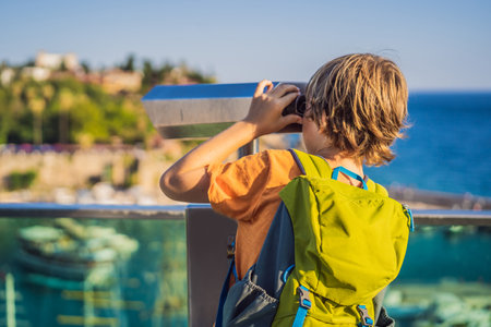 Boy tourist looks through binoculars in Old town Kaleici in Antalya. Turkiye. Panoramic view of Antalya Old Town port, Taurus mountains and Mediterrranean Sea, Turkey. Traveling with kids conceptの写真素材