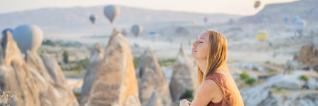 BANNER, LONG FORMAT Tourist woman looking at hot air balloons in Cappadocia, Turkey. Happy Travel in Turkey concept. Woman on a mountain top enjoying wonderful viewの写真素材