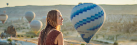 BANNER, LONG FORMAT Tourist woman looking at hot air balloons in Cappadocia, Turkey. Happy Travel in Turkey concept. Woman on a mountain top enjoying wonderful viewの写真素材