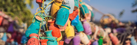 BANNER, LONG FORMAT Wish tree. Small multi-colored jugs with inscriptions, wishes hanging on the branches of a tree., against the backdrop of sand ruins and blue skyの写真素材