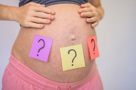 Choosing baby name. Confused pregnant woman with question marks on paper stickers on tummy