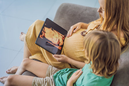 Mom and her son looking on ultrasound image of his unborn baby brother on mothers tablet. Concept of...