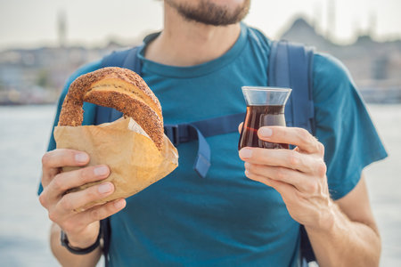 Man in Istanbul having breakfast with Simit and a glass of Turkish tea. Glass of Turkish tea and bagel Simit against golden horn bay in Istanbul, Turkey. Turkiyeの写真素材