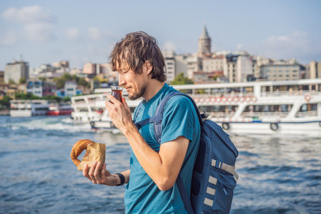 Man in Istanbul having breakfast with Simit and a glass of Turkish tea. Glass of Turkish tea and bagel Simit against golden horn bay and the Galata Tower in Istanbul, Turkey. Turkiyeの写真素材