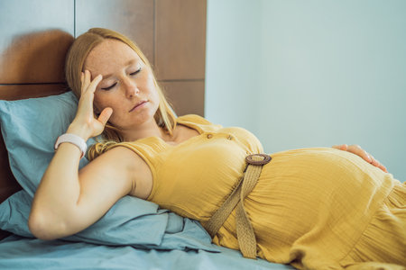 A stressed tired pregnant mother lying in bed at home. Morning sickness and nauseaの写真素材
