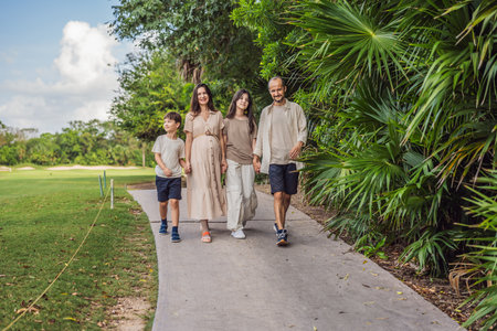 A loving family enjoying a leisurely walk in the park - a radiant pregnant woman after 40, embraced by her husband, and accompanied by their adult teenage children, savoring precious moments together amidst natures beauty. Pregnancy after 40 conceptの写真素材