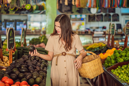 A glowing pregnant woman after forty makes a healthy choice as she selects organic vegetables and fruits at the vibrant organic market, prioritizing her well-being and her babys healthの写真素材