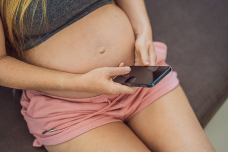Pregnant girl with a smartphone. The concept of a negative impact on the unborn child in the womb. Violation of the nervous system of the child, reproductiveの写真素材
