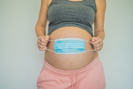 Belly of a pregnant woman holding medical mask close upの写真素材