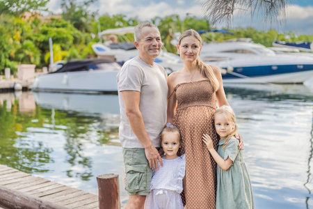 A happy, mature couple over 40 with their two daughters enjoying a leisurely walk on the waterfront, their joy evident as they embrace the journey of pregnancy later in lifeの写真素材