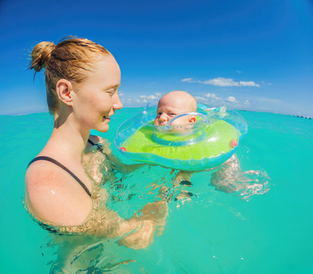 Adorable baby swims in an inflatable ring around his neck, enjoying the sea with his mom.の写真素材