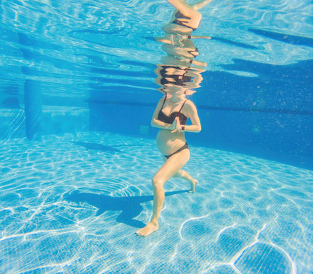 Embracing aquatic fitness, a pregnant woman demonstrates strength and serenity in underwater aerobics, creating a serene and empowering image in the poolの写真素材