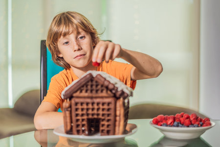 Immerse in festive delight as a boy crafts boy crafting an unconventional gingerbread house, infusing Christmas with unique creativity and festive cheer. A sweet scene of seasonal bonding and culinary funの写真素材