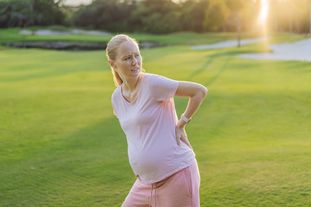 Expectant woman experiences back pain outdoors, seeking relief and comfort during pregnancy with a...