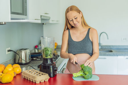 Embracing a nutritious choice, a pregnant woman joyfully prepares a vibrant vegetable smoothie,...