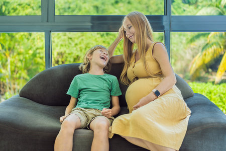 Pregnant mother and son are talking and spending time together at home. Little child boy looking at...
