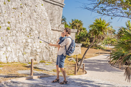 Father and son tourists enjoying the view Pre-Columbian Mayan walled city of Tulum, Quintana Roo, Mexico, North America, Tulum, Mexico. El Castillo - castle the Mayan city of Tulum main templeの写真素材