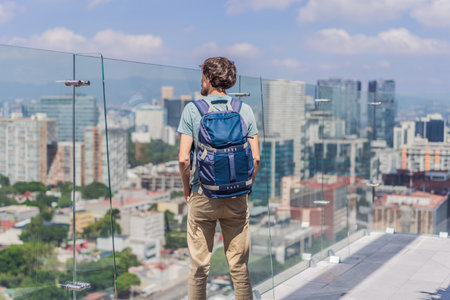 Male tourist or businessman standing on a skyscraper rooftop with a panoramic view of Mexico City. Travel or international business in Mexico conceptの写真素材