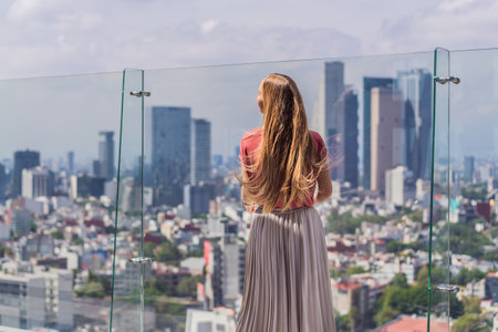 Female tourist or businesswoman standing on a skyscraper rooftop with a panoramic view of Mexico City. Travel or international business in Mexico conceptの写真素材
