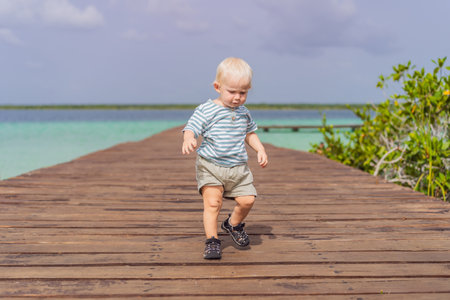Little baby toddler exploring wooden pier over the turquoise waters of Bacalar Lake, Mexico....